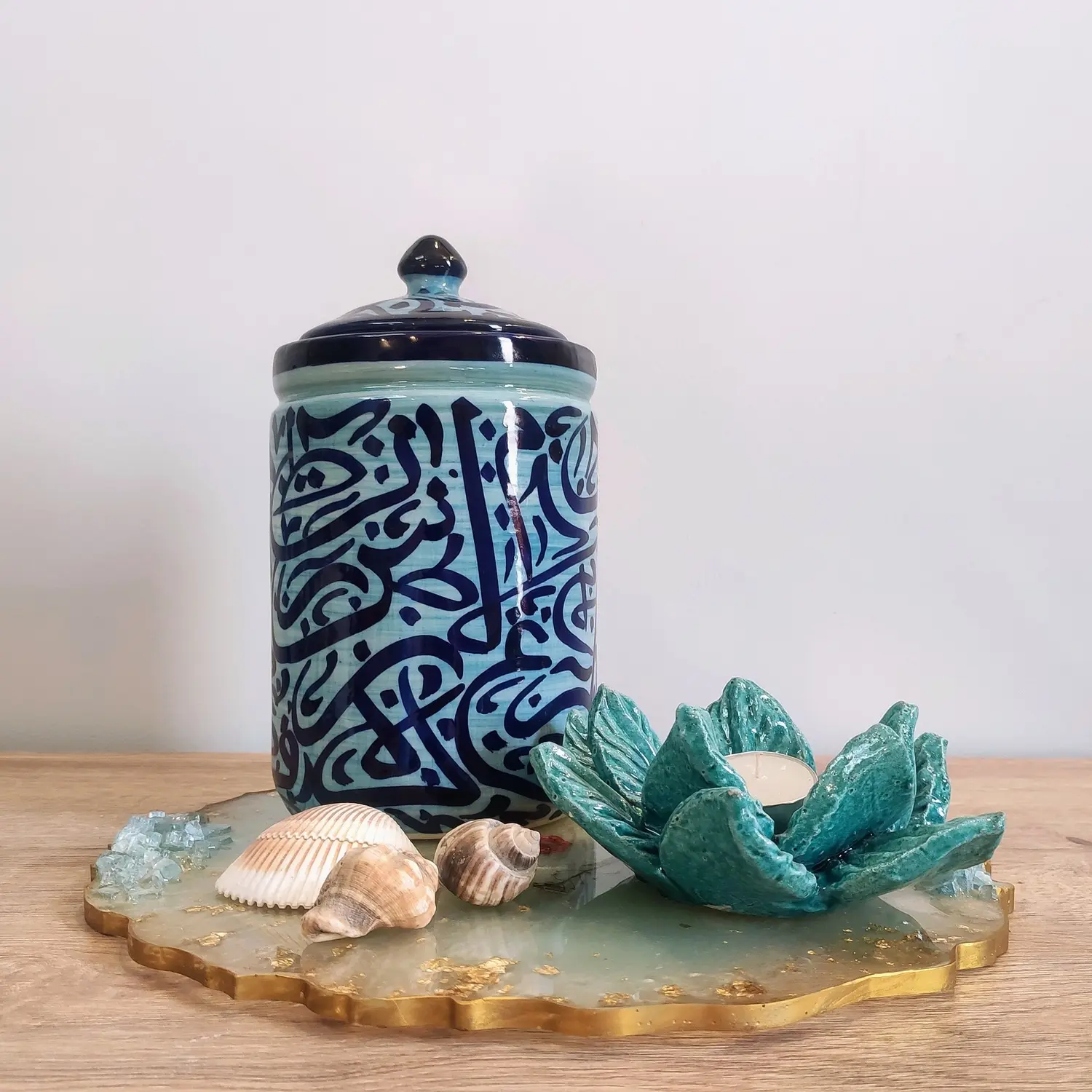 A light blue ceramic jar with dark blue Arabic calligraphy.