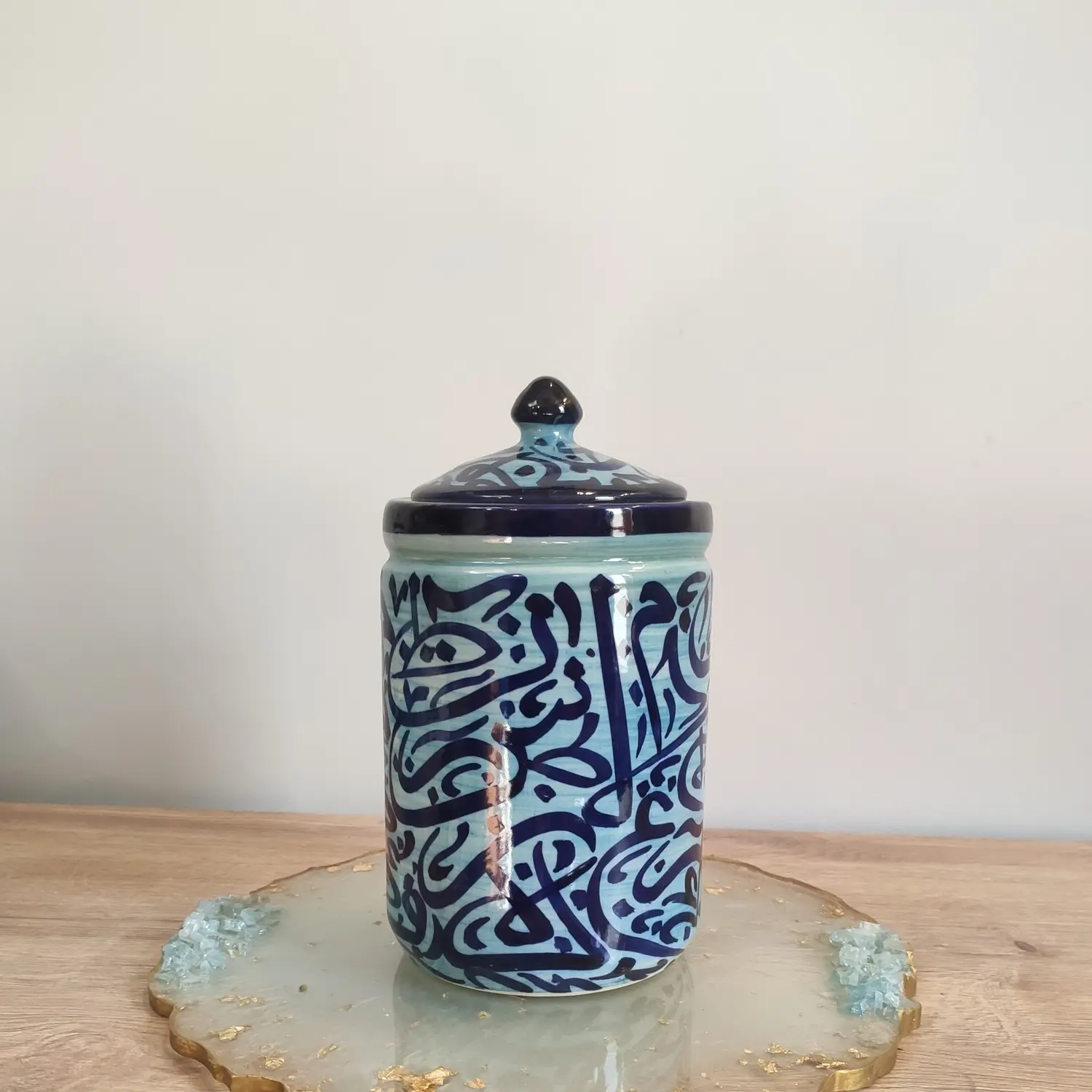 A light blue ceramic jar with dark blue Arabic calligraphy.