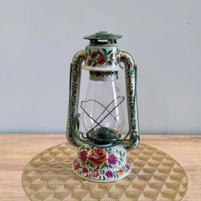 Hand-painted vintage metal lantern with multicolor floral patterns on a soft green base, featuring a clear glass chamber and classic frame.