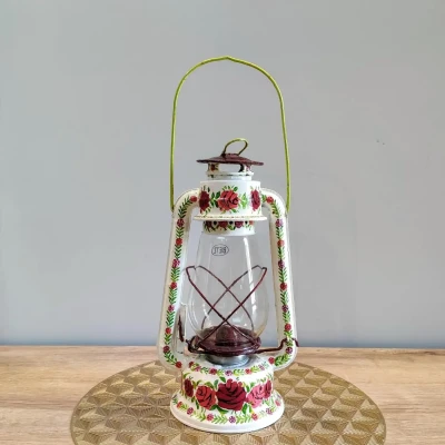Hand-painted metal lantern with red rose motifs on a white base, featuring a clear glass chamber and vintage-style handle.
