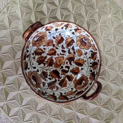 Brown Multani pottery serving karahi with floral patterns and side handles, placed on a gold geometric-patterned mat.