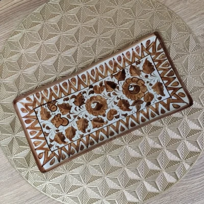 Rectangular brown Multani pottery dish with floral patterns, placed on a gold geometric-patterned mat.