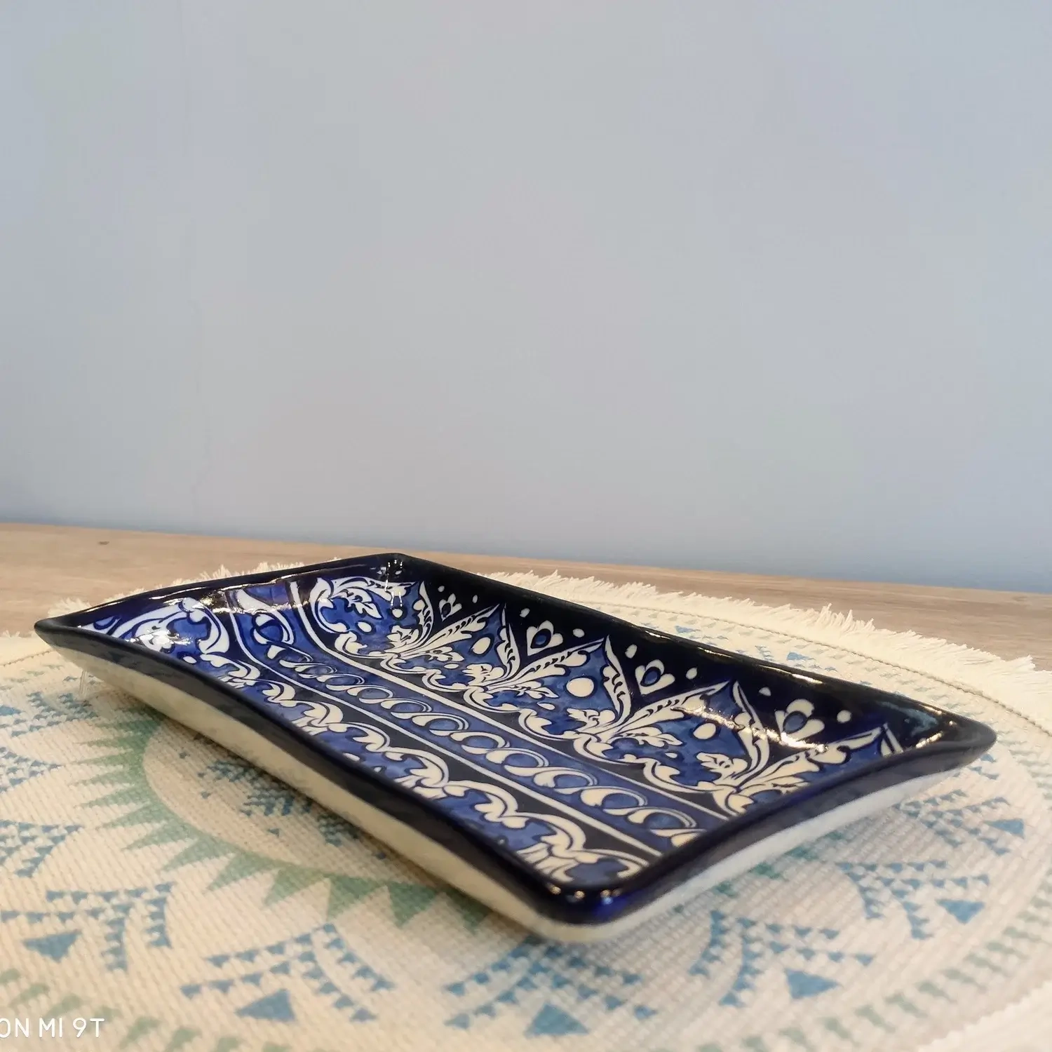 Dark blue Multani pottery rectangular dish with white floral and vine motifs, placed on a patterned woven mat.