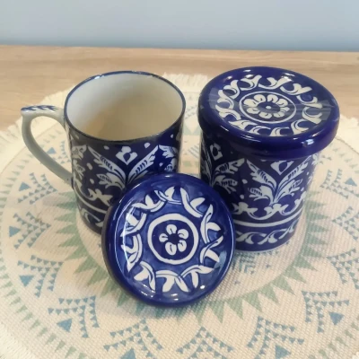 Blue and white Multani pottery mug and storage jar with lids, displayed on a patterned woven mat.