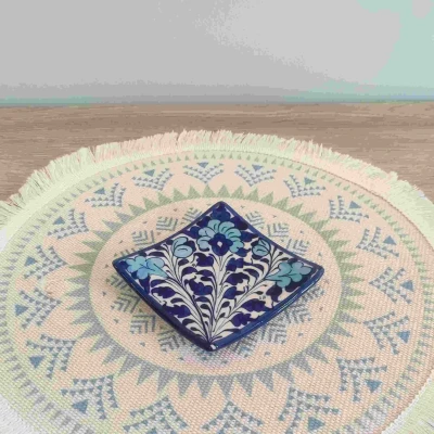 Blue Multani pottery square coaster with light blue floral patterns, displayed on a patterned woven mat.
