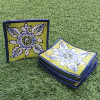 Set of green Multani pottery square coasters with blue-and-white floral designs, displayed on grass.