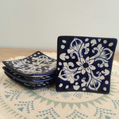 Set of four blue Multani pottery square coaster plates with white floral designs, arranged on a patterned woven mat.