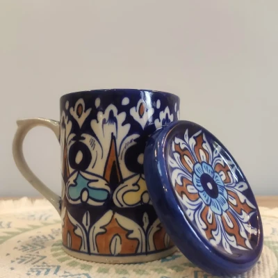 Multicolored Multani pottery mug with a matching floral lid, displayed on a patterned woven mat.