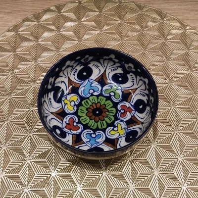 Multicolored Multani pottery bowl with floral motifs, placed on a gold geometric-patterned mat.