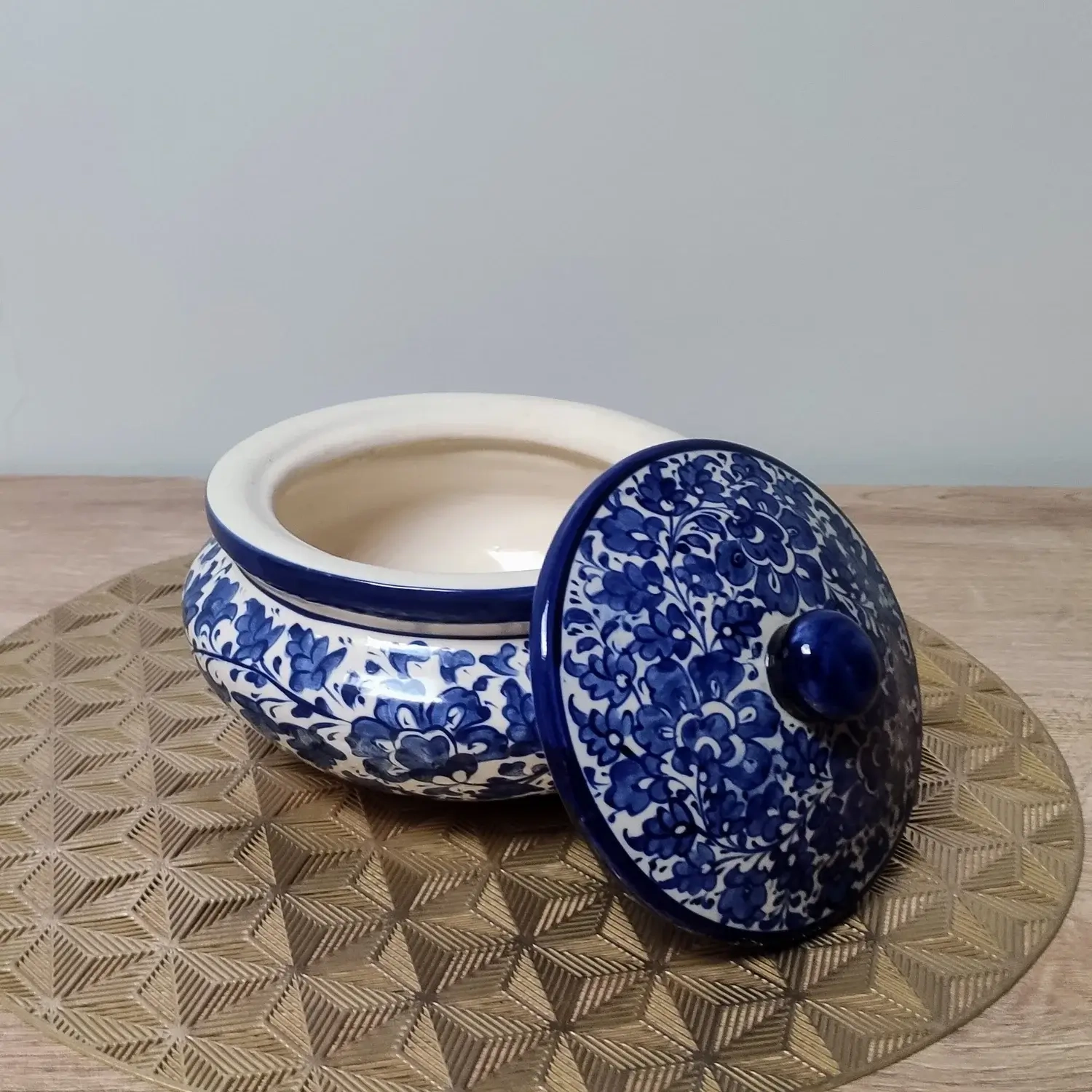 Blue and white Multani pottery handi with a floral-patterned lid, displayed on a gold geometric-patterned mat.
