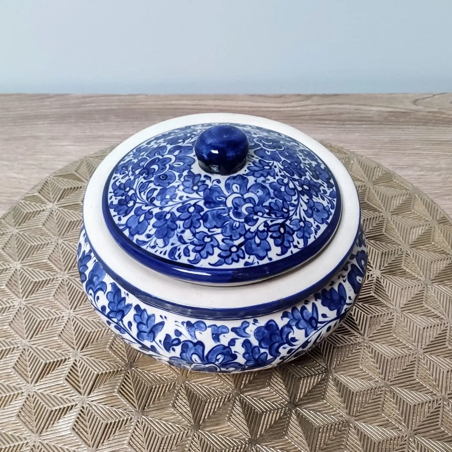 Blue and white Multani pottery handi with a floral-patterned lid, displayed on a gold geometric-patterned mat.