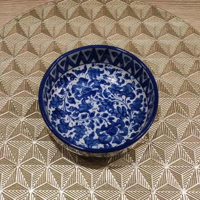 Blue and white Multani pottery bowl with intricate floral designs, displayed on a gold geometric-patterned mat.