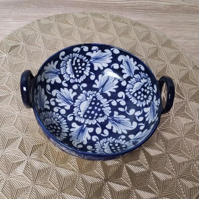 Blue Multani pottery serving karahi with white floral patterns and side handles, placed on a gold geometric-patterned mat.
