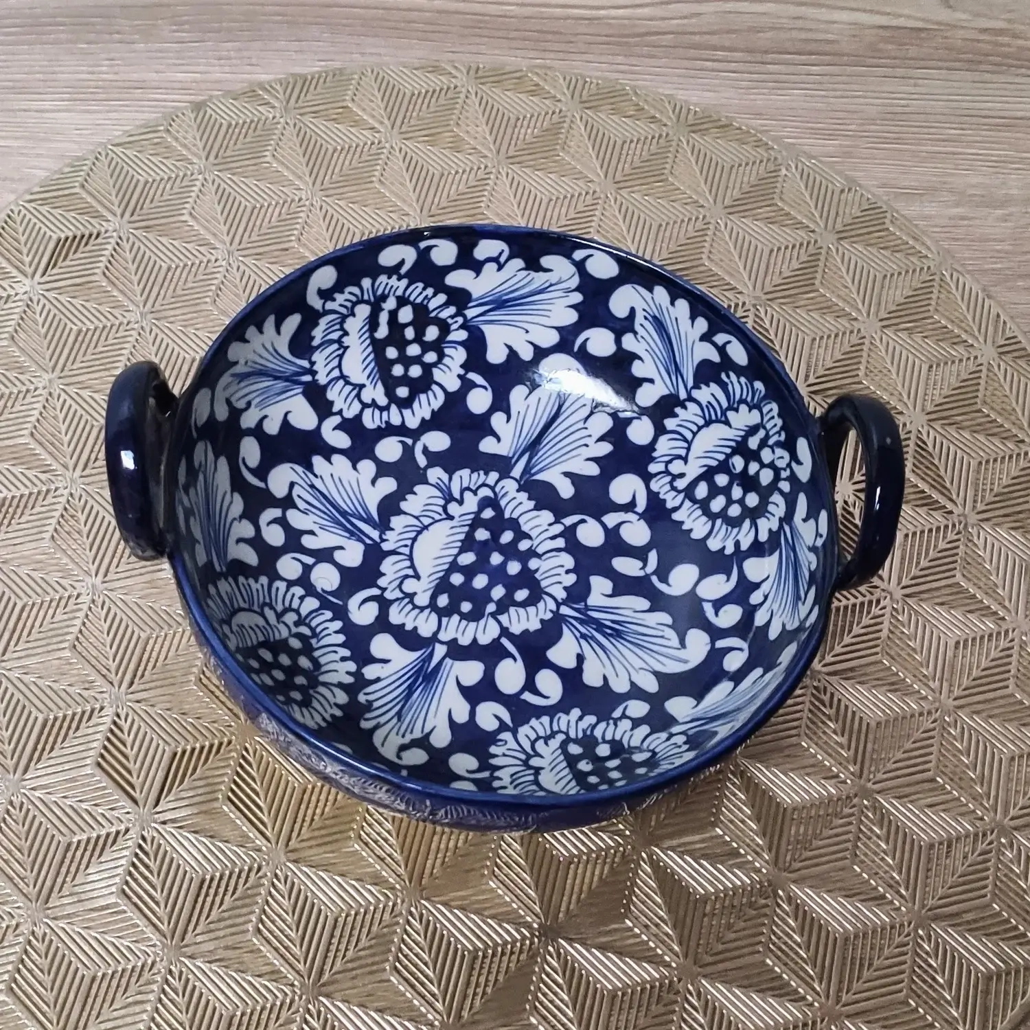 Blue Multani pottery serving karahi with white floral patterns and side handles, placed on a gold geometric-patterned mat.