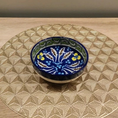 Multicolored Multani pottery bowl with blue, green, and yellow floral motifs, displayed on a gold geometric-patterned mat.