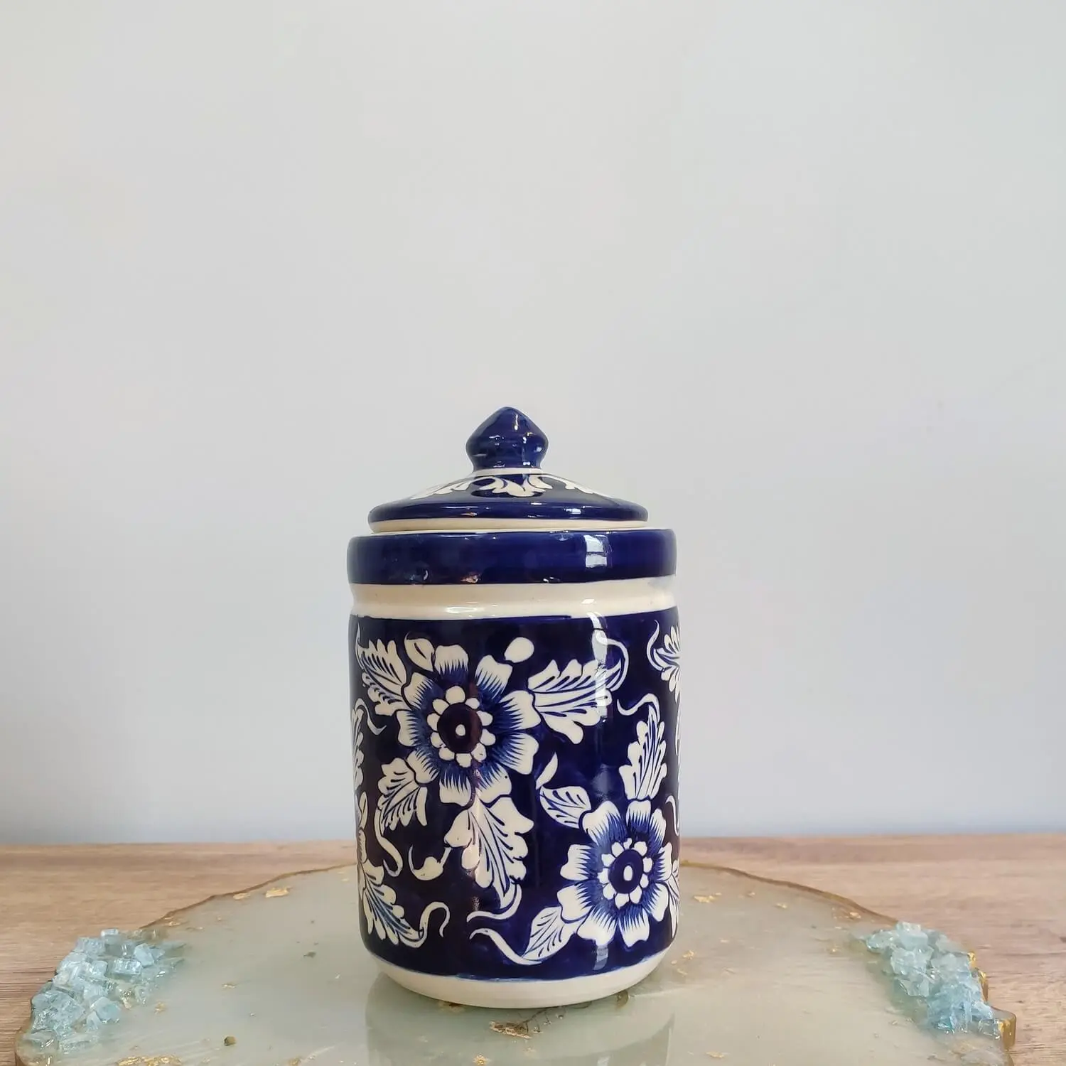 Medium-sized navy blue Multani pottery jar with a matching lid, featuring hand-painted white Gul Daudi floral patterns, displayed on a decorative resin base.