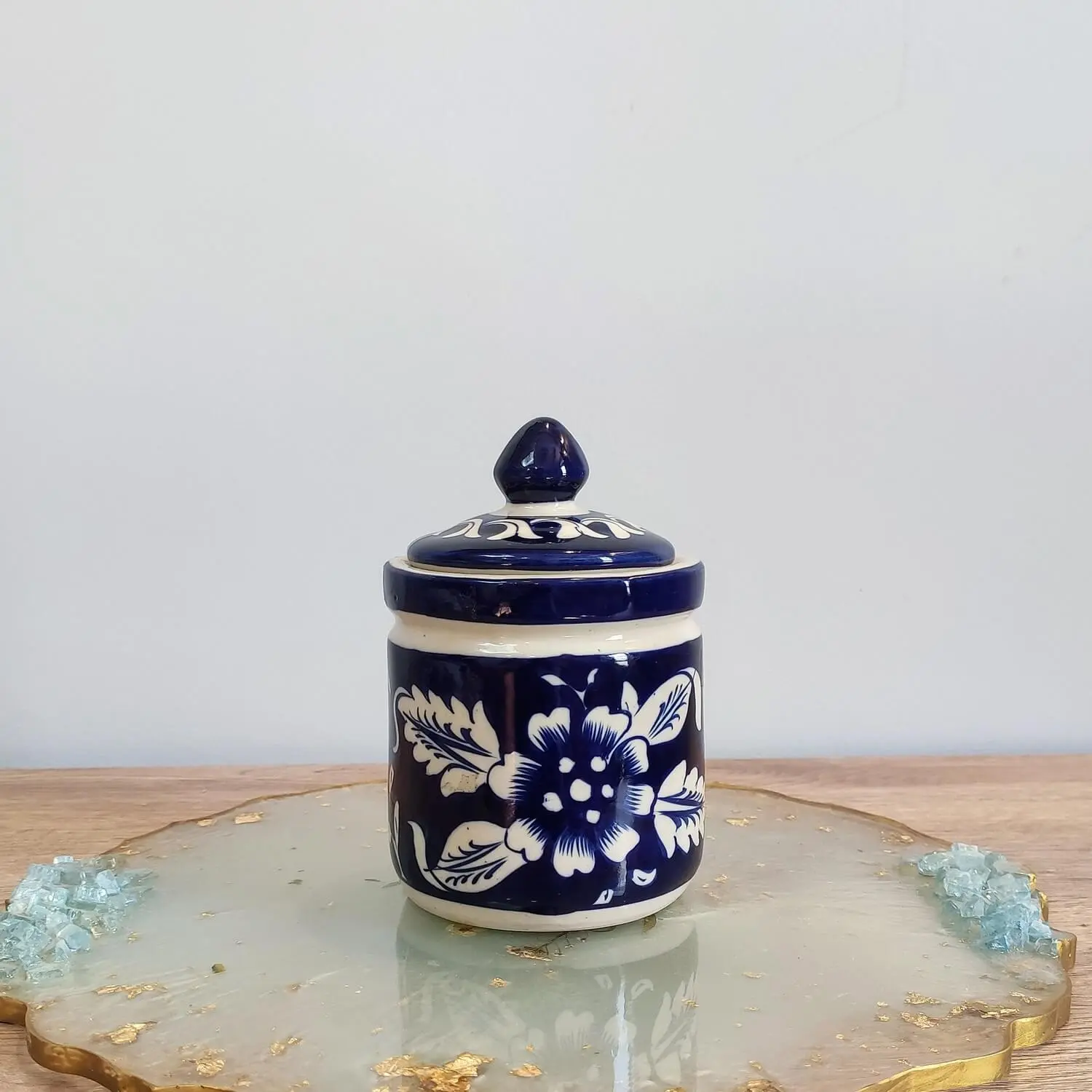Small navy blue Multani pottery jar with a pointed lid, adorned with white Gul Daudi floral motifs, styled on a resin display board.