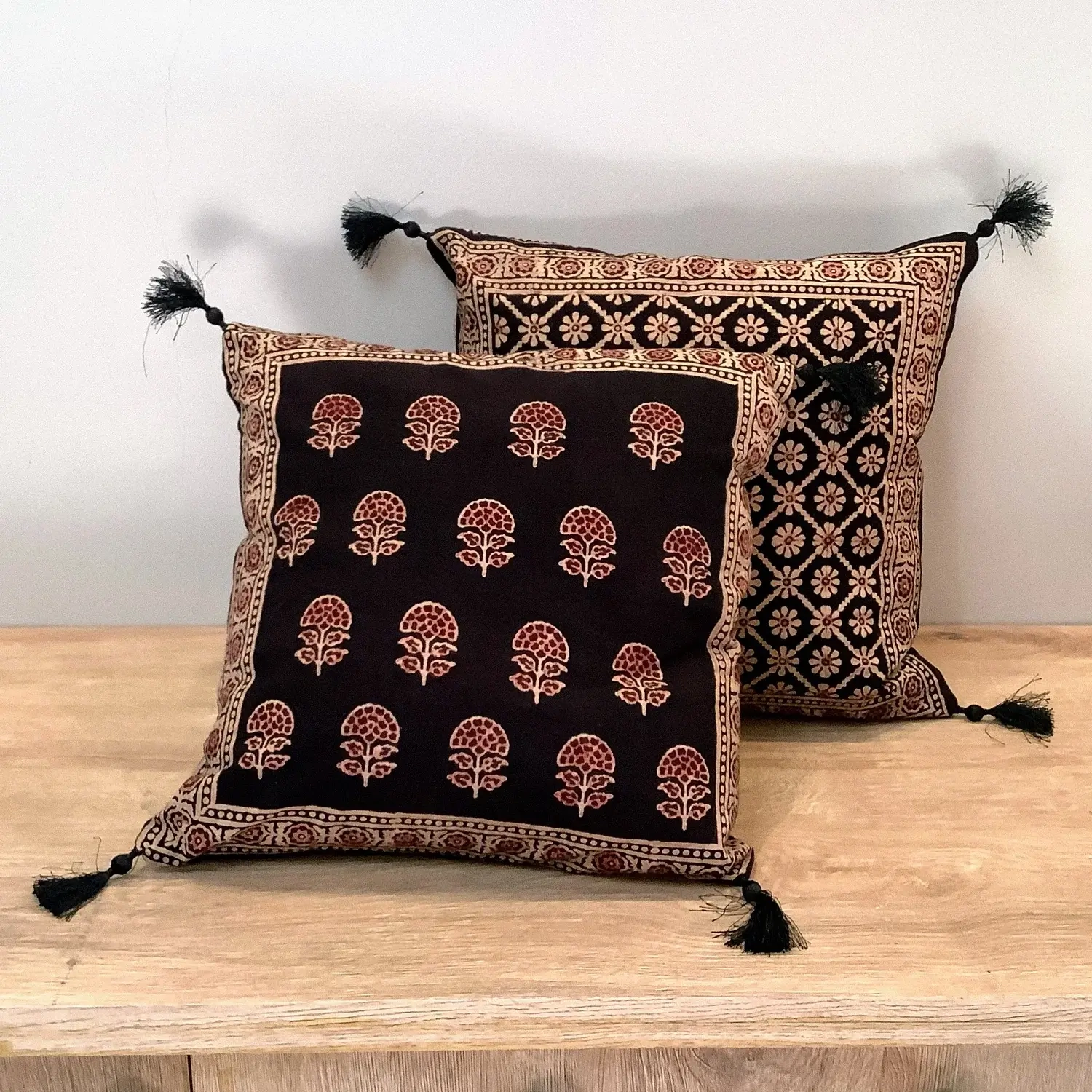 Ajrak block print black floral booti double-sided cushion covers with tassels displayed on a wooden surface.