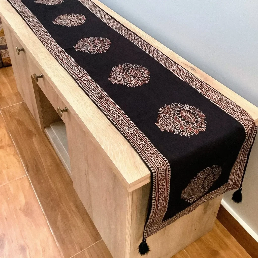 Ajrak and block print black floral table runner with traditional motifs displayed on a wooden console.