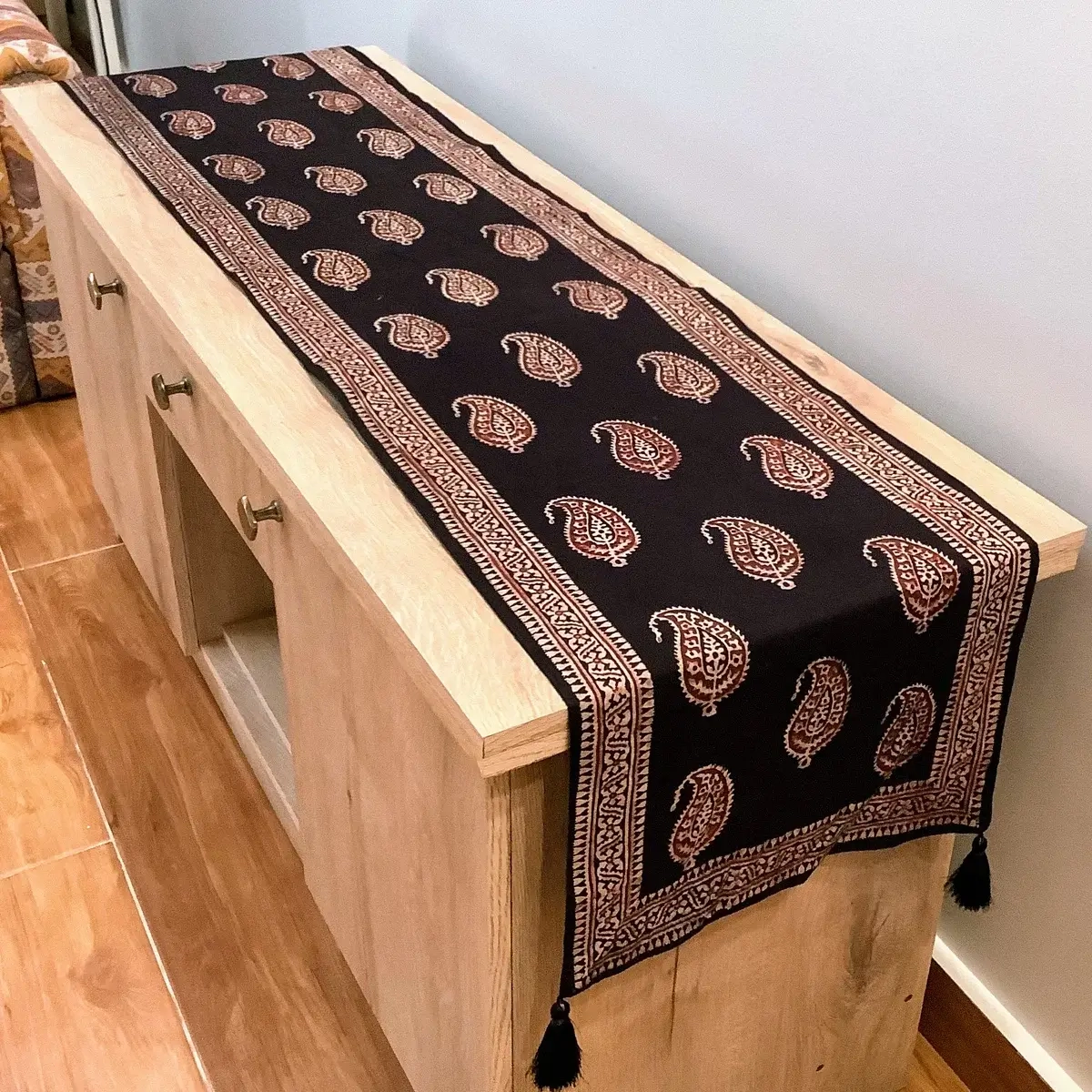 Ajrak and block print black Keri table runner with paisley motifs displayed on a wooden console.