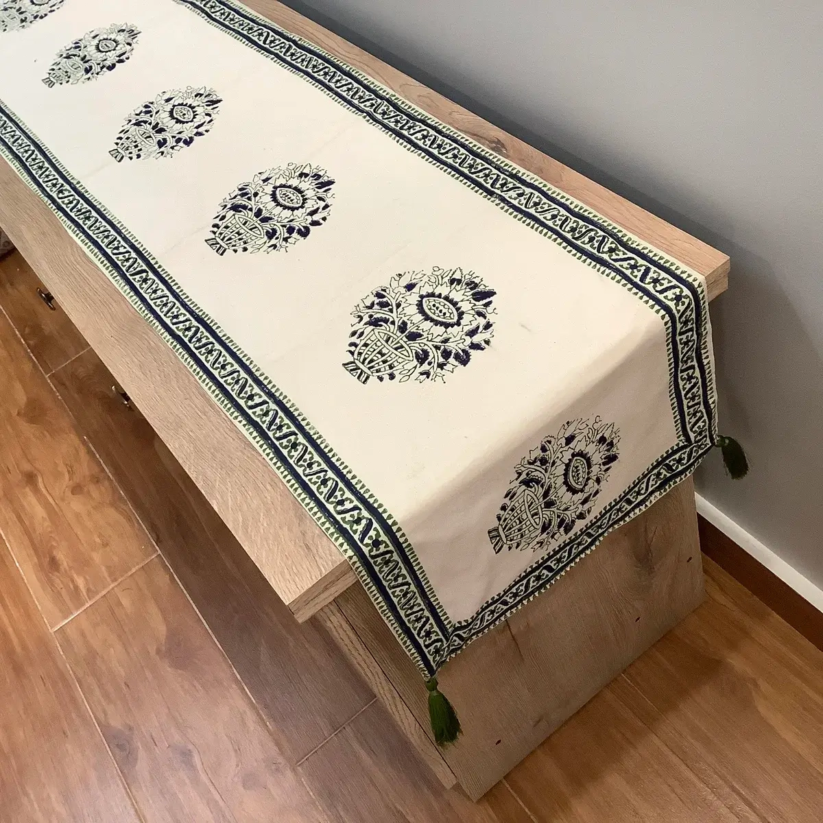 Ajrak and block print off-white table runner with green and blue floral medallion motifs displayed on a wooden console.