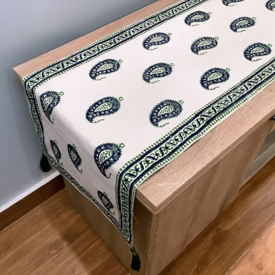Off-white Ajrak block print table runner with green and blue Keri paisley motifs displayed on a wooden surface.