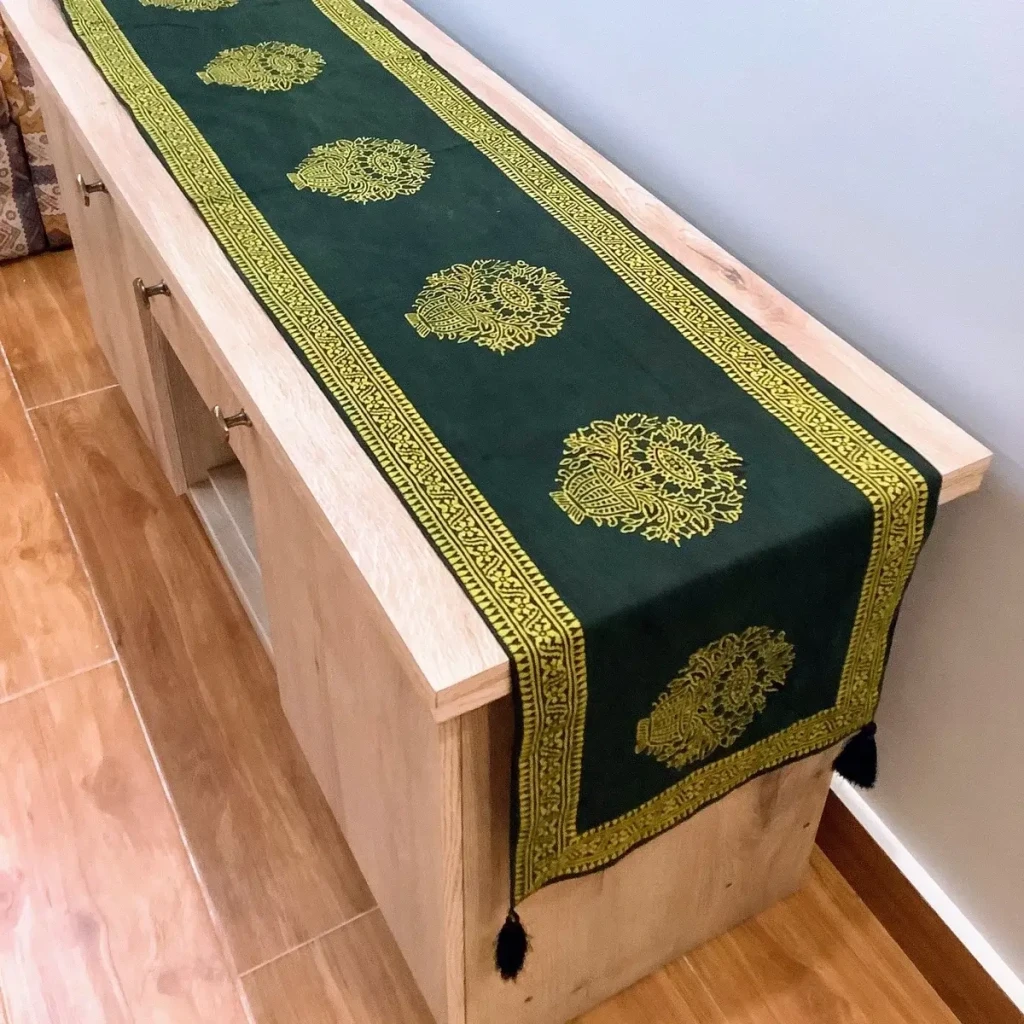 Green Ajrak block print table runner with floral motifs and traditional borders displayed on a wooden console.