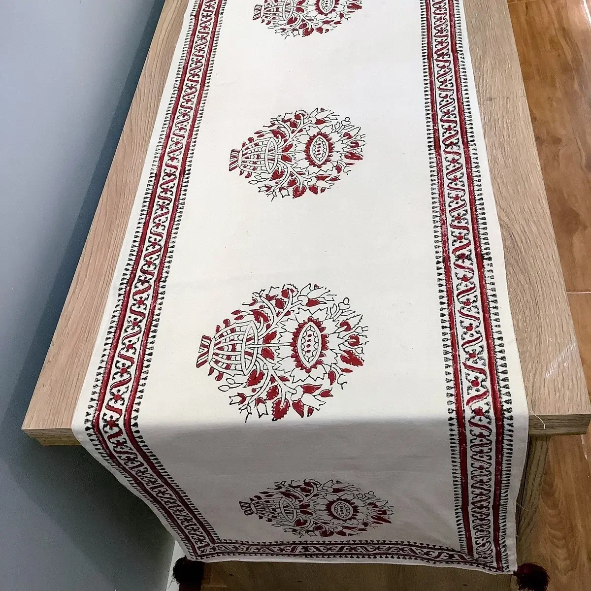 Top view of red and white floral block print table runner with traditional borders and tassels.