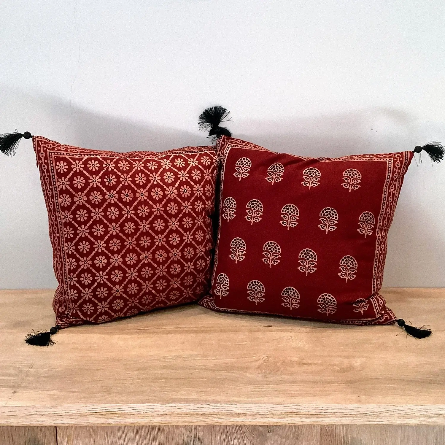 Double-sided Ajrak cushion cover featuring red floral booti motifs on one side and a geometric floral pattern on the other.
