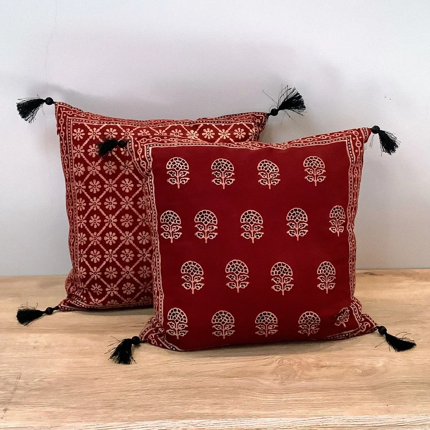 Ajrak block print red floral booti double-sided cushion covers with tassels displayed on a wooden surface.